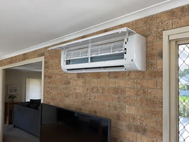 Clean split system with open front panel and visible filters on a brick living room wall in Upper Coomera