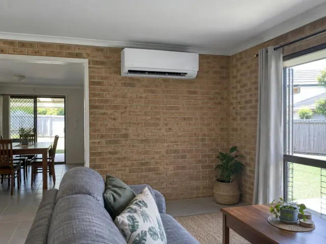 Clean wall-mounted split system on a brick feature wall in a living room with tiled floors in Upper Coomera