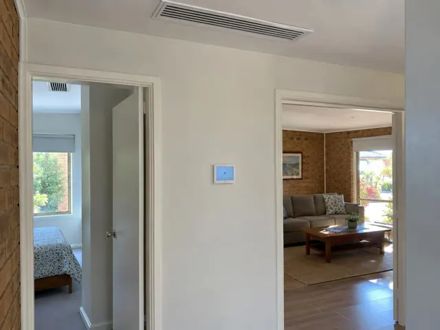 Ceiling ducted air grille and wall controller in a home interior with open doorways in Helensvale