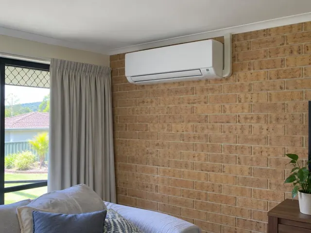 Wall-mounted split system indoor unit on a brick feature wall in a living room in Oxenford